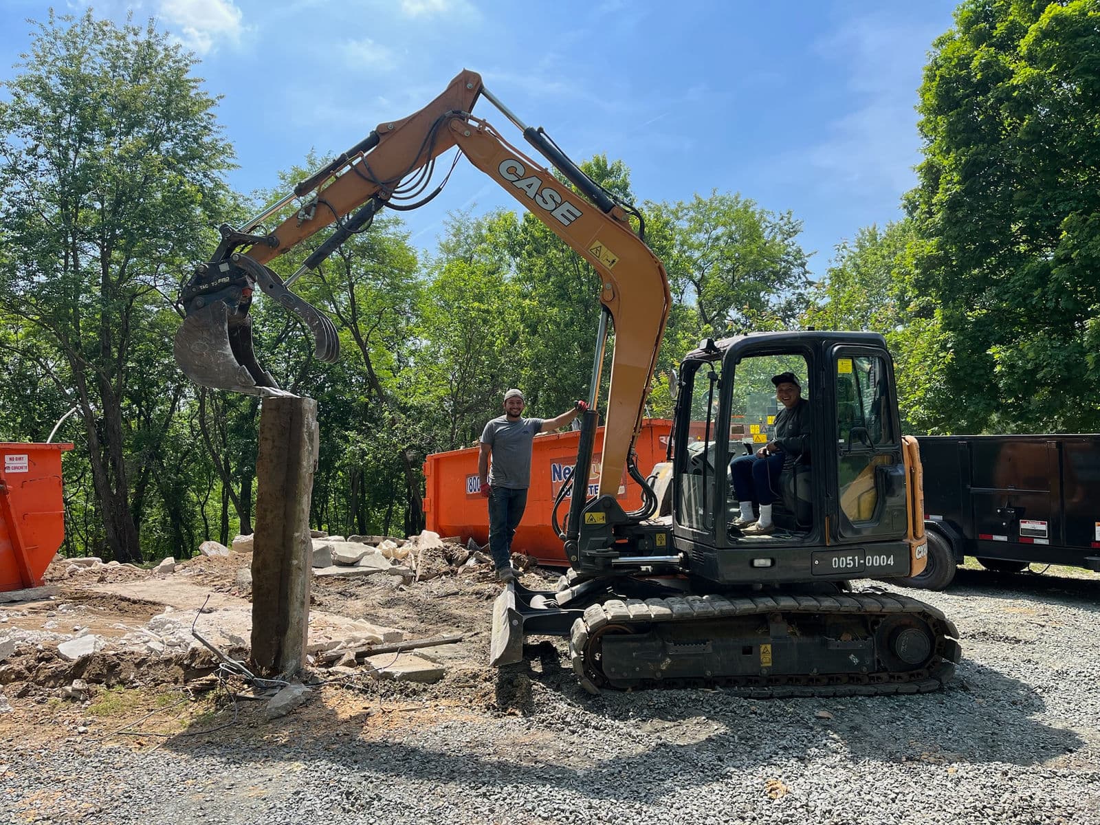 Excavator breaking out concrete with dumpsters behind